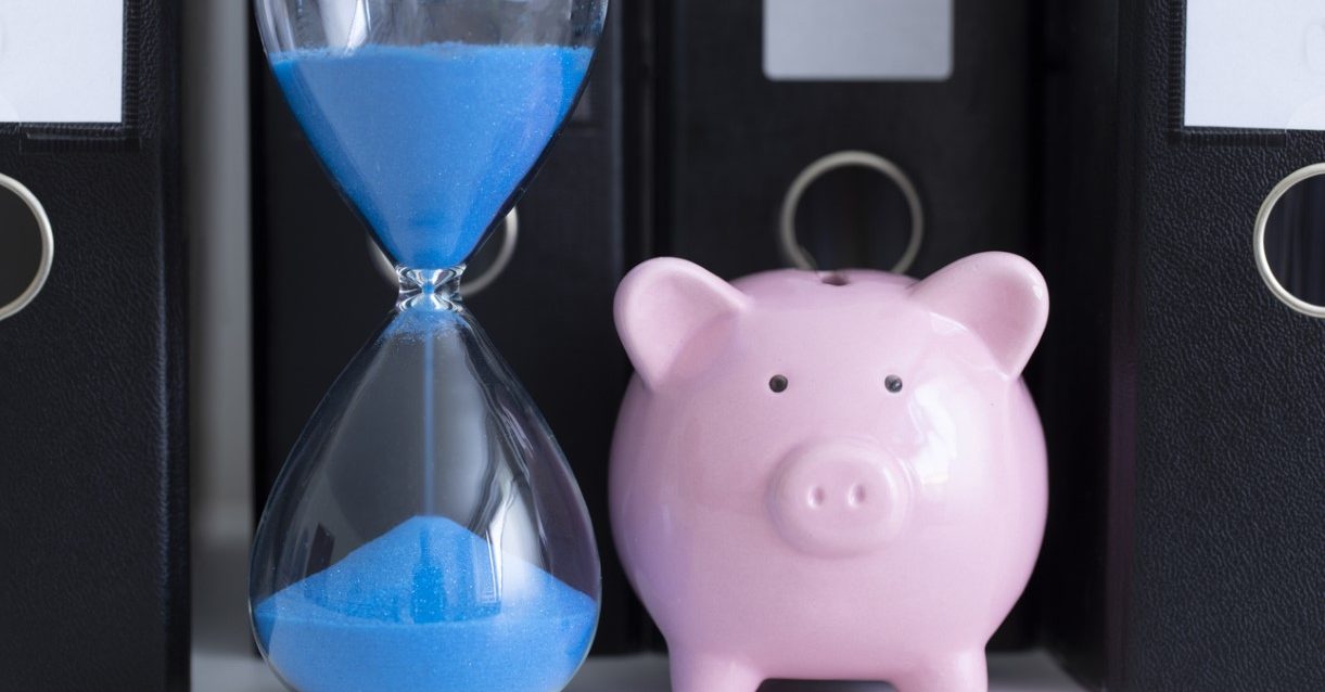 Blue hourglass and a piggy bank in front of a row of office folders Blue hourglass and a piggy bank in front of a row of office folders