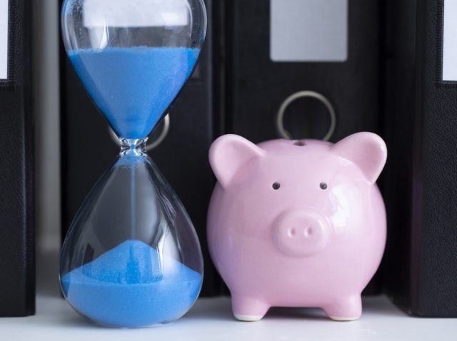 Blue hourglass and a piggy bank in front of a row of office folders Blue hourglass and a piggy bank in front of a row of office folders